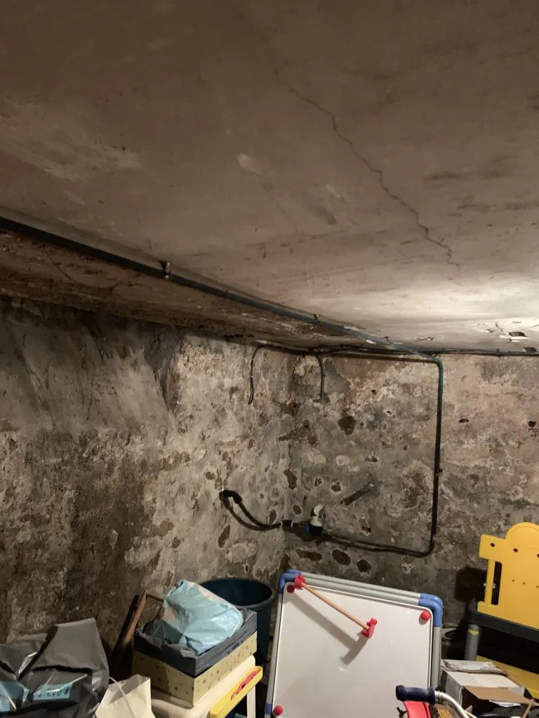 Cave avant travaux avec murs en pierre, matériel entreposé et plafond brut