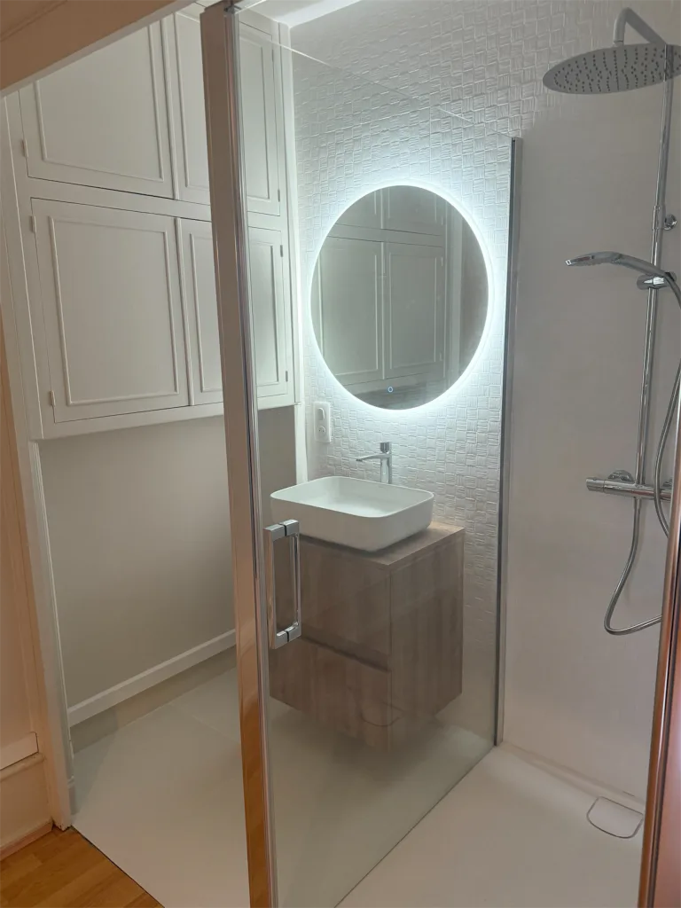 Vue rapprochée de la douche vitrée et du miroir rond éclairé dans la salle d’eau