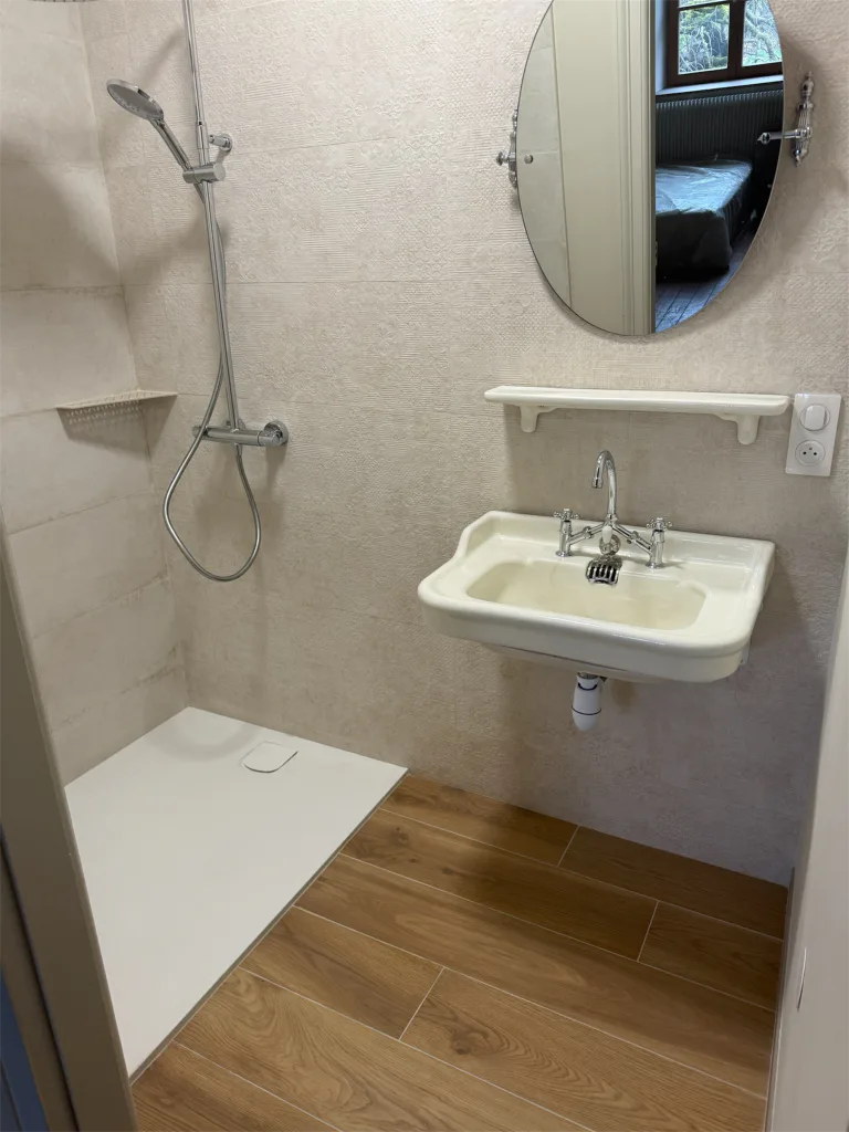 Petite salle d’eau terminée avec douche ouverte, vasque suspendue et miroir ovale