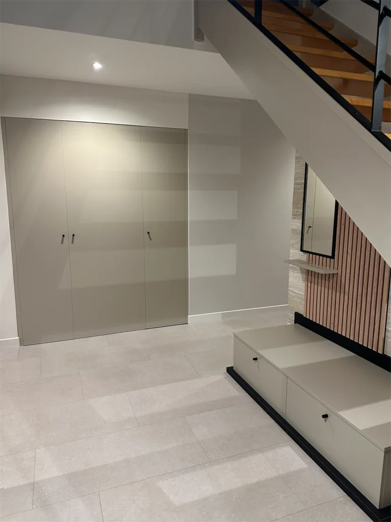 Entrée rénovée avec placard taupe, marches claires et habillage à tasseaux sous l’escalier