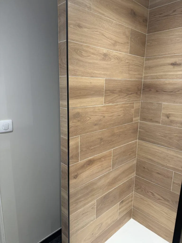Détail d’une douche avec carrelage imitation bois et paroi vitrée à profil noir