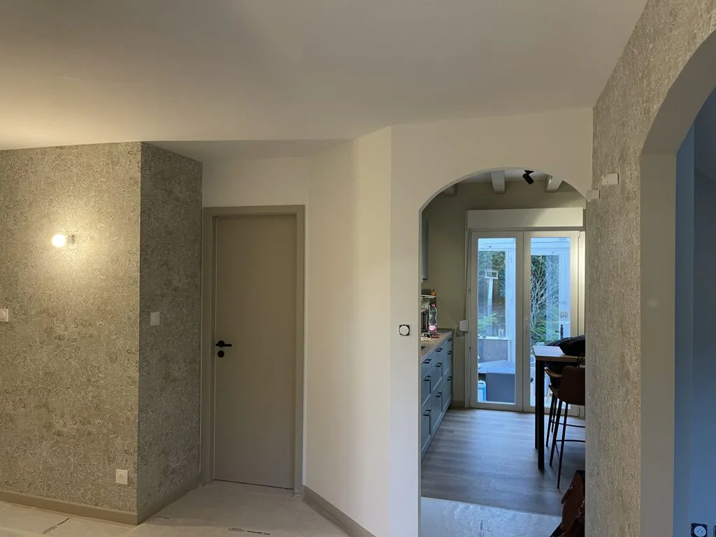 Couloir rénové avec murs texturés et ouverture arrondie vers la cuisine