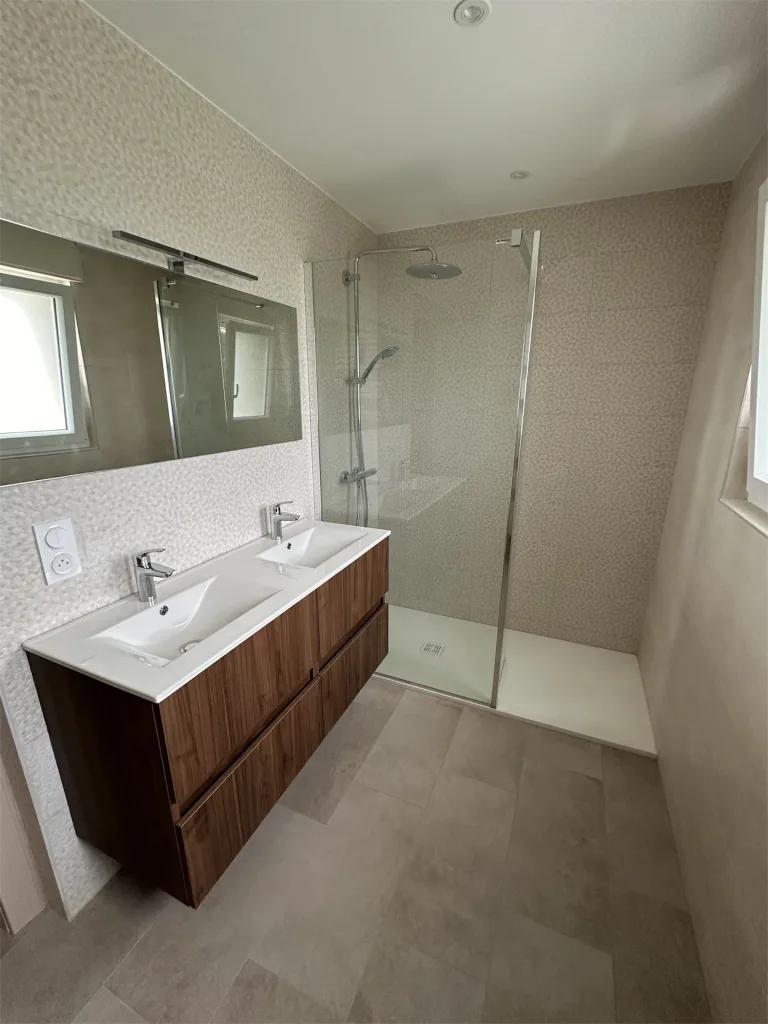 Salle d’eau avec meuble à deux vasques, miroir et douche vitrée sur carrelage beige