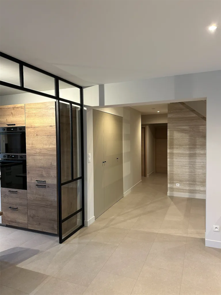 Verrière noire séparant la cuisine de l’entrée et du couloir carrelé
