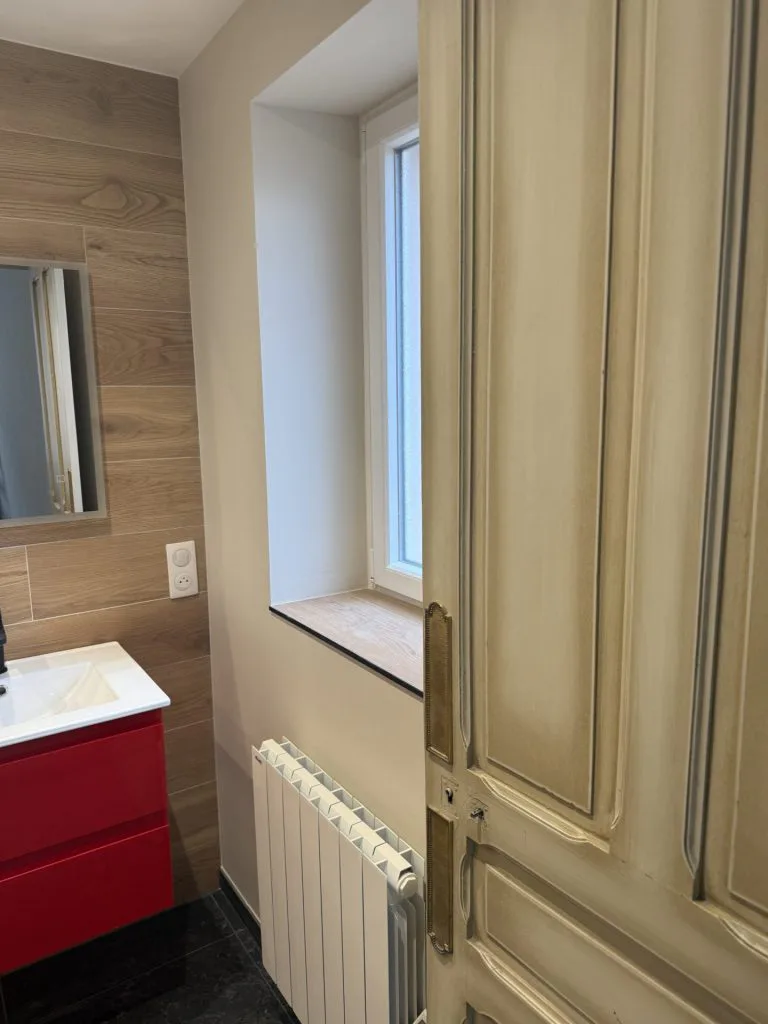 Salle d’eau avec meuble vasque rouge, fenêtre et carrelage mural imitation bois
