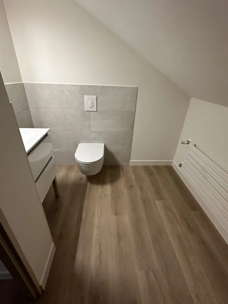 Toilettes rénovées avec cuvette suspendue, soubassement gris et sol imitation bois