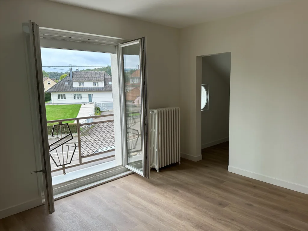 Pièce rénovée avec porte-fenêtre ouverte sur le balcon et sol imitation bois