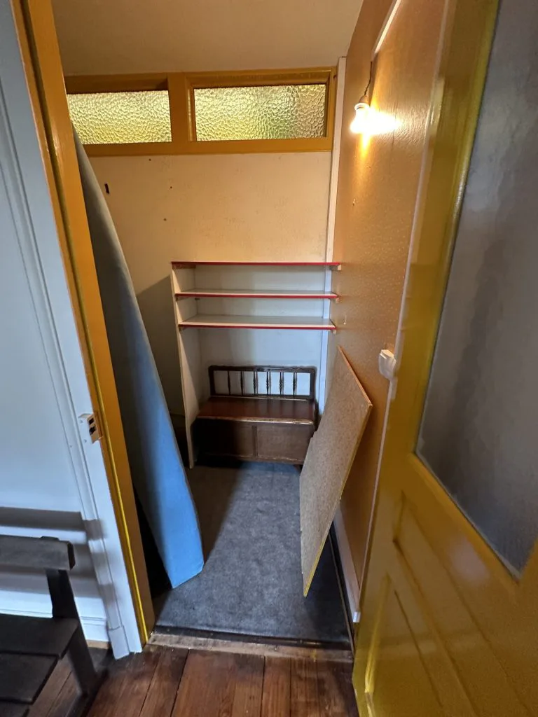 Ancien réduit sous une imposte vitrée, avec étagères et chaise en bois