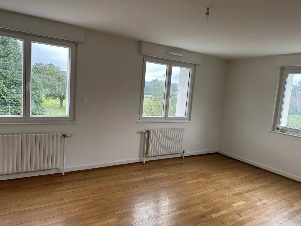 Pièce de vie vide après rénovation avec parquet, murs clairs et trois fenêtres