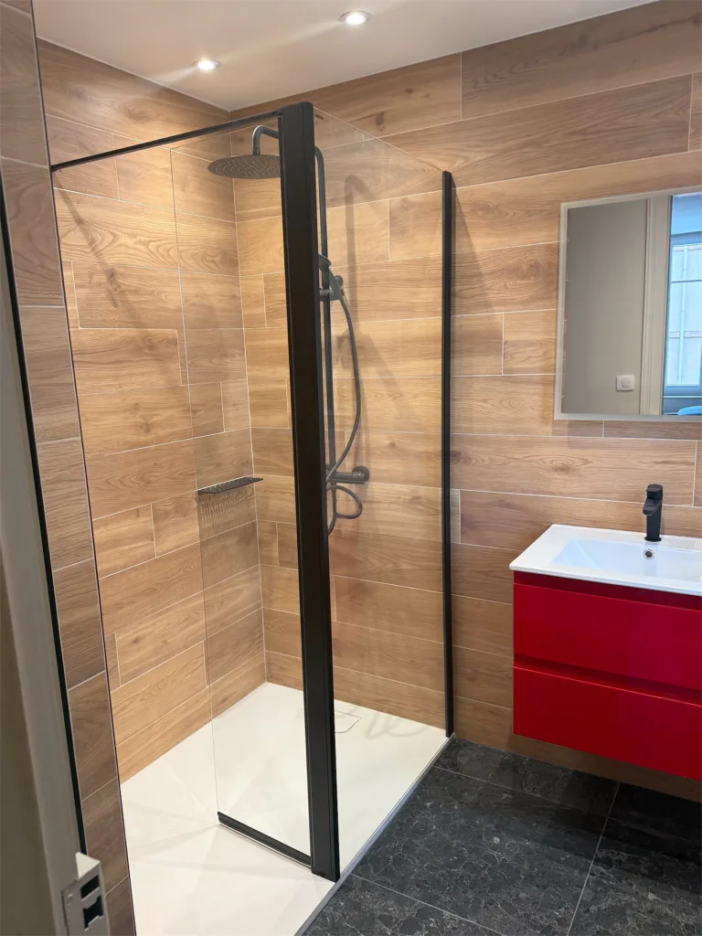 Douche vitrée à cadre noir et meuble vasque rouge sous un plafond à spots