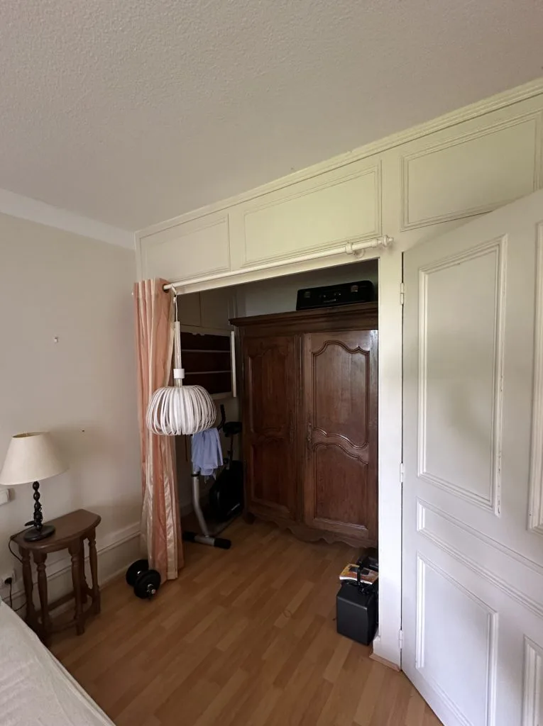 Chambre avant travaux avec parquet, placards clairs et passage vers une armoire ancienne