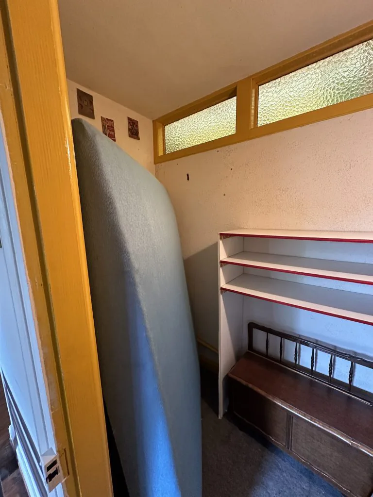 Vue de l’intérieur du réduit avant travaux, avec étagères murales et sol sombre