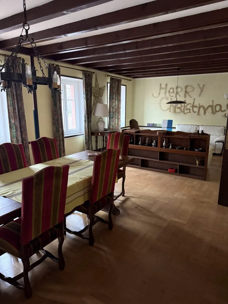 Salle à manger avant travaux avec poutres brunes, table et chaises rouges