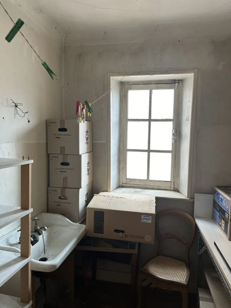 Pièce à transformer en salle d’eau, avec ancien lavabo, cartons et fenêtre