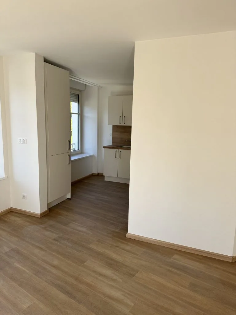 Appartement rénové avec cuisine blanche ouverte sur une pièce au sol imitation bois