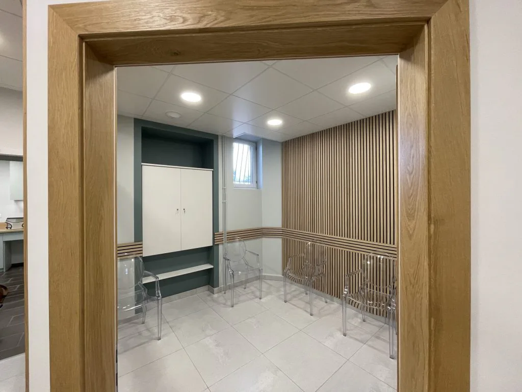 Vue de la salle d’attente à travers une porte en bois et une cloison vitrée
