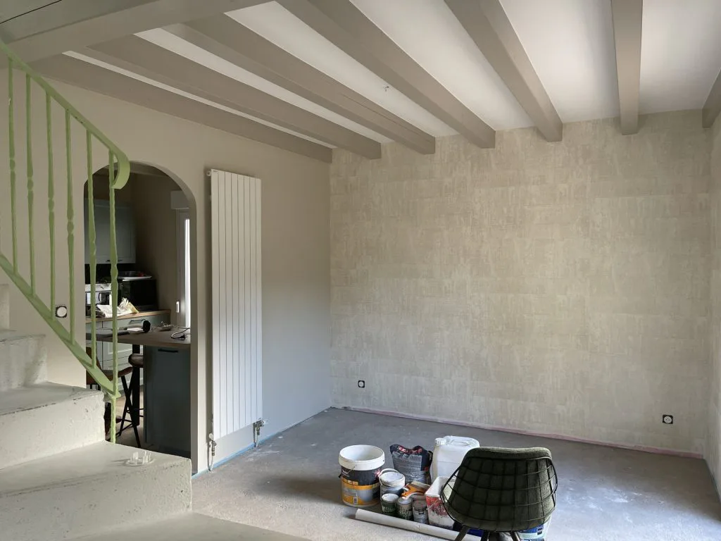 Pièce de vie en travaux avec poutres blanches, pots de peinture et escalier en préparation