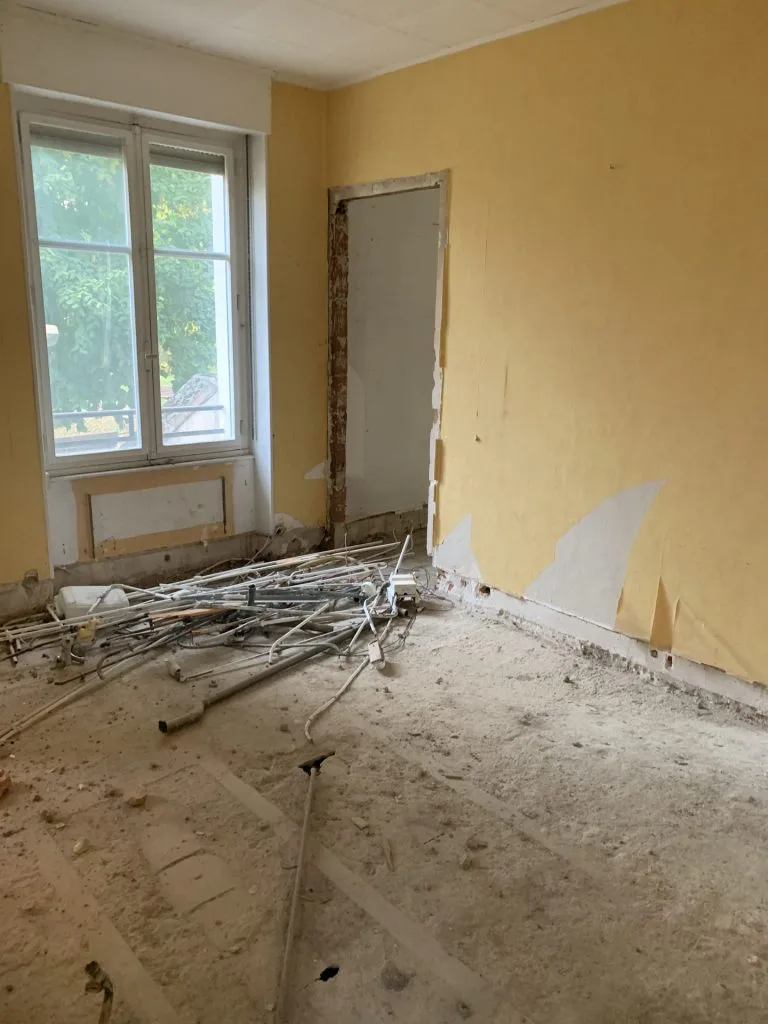 Pièce en démolition avec gravats au sol et ancien revêtement mural jaune