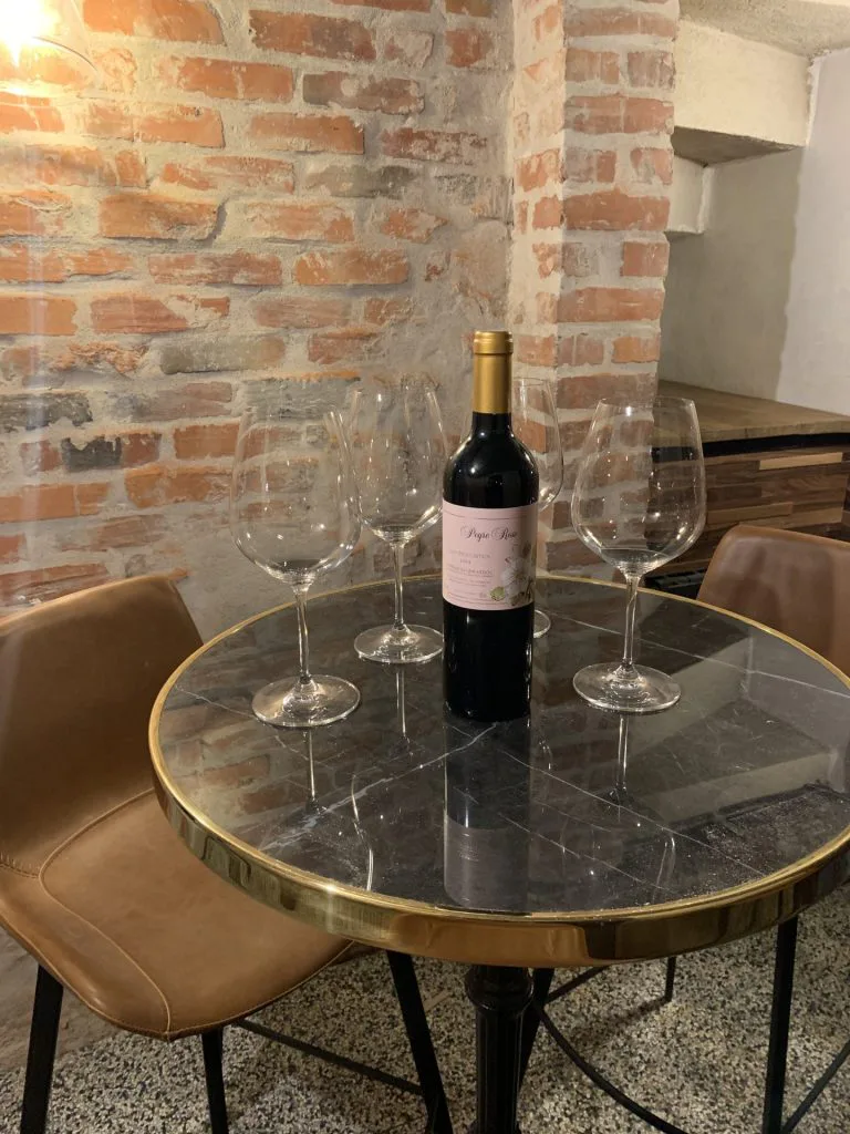 Table ronde de dégustation avec bouteille, verres et fauteuils devant un mur en briques