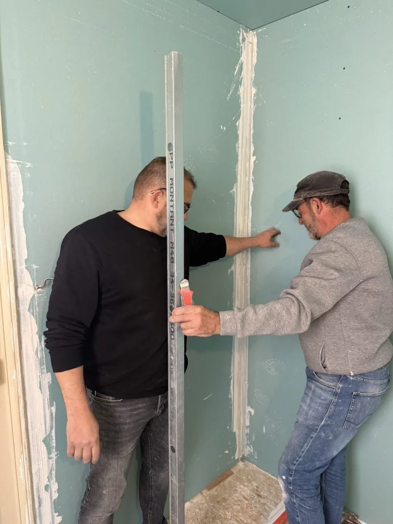 Deux personnes contrôlant une cloison de plaques de plâtre avec une règle pendant les travaux