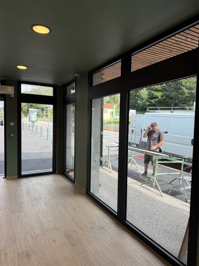Entrée vitrée de la boulangerie avec menuiseries noires et sol imitation bois