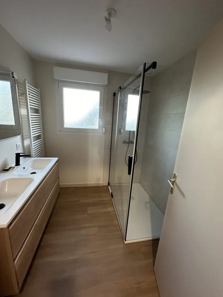 Salle d’eau rénovée avec double vasque en bois, douche vitrée et sèche-serviettes blanc