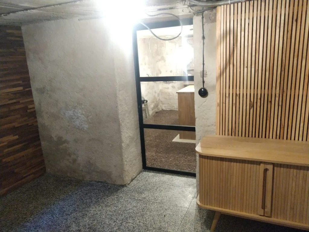 Entrée de la cave à vin avec porte vitrée noire et buffet devant des tasseaux de bois