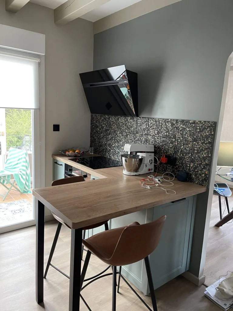 Coin repas de la cuisine avec plan de travail en bois, tabouret et hotte noire