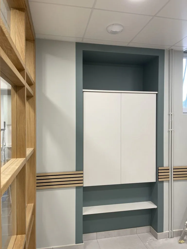 Espace d’attente avec placard blanc, banc et cloison vitrée à ossature bois