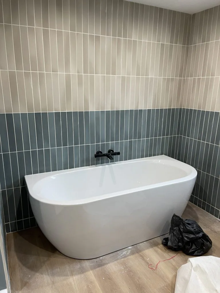 Baignoire îlot devant un mur de carrelage vertical gris-vert pendant les finitions