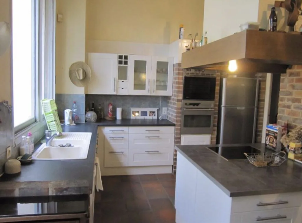 Cuisine avant travaux avec meubles blancs et habillage en briques