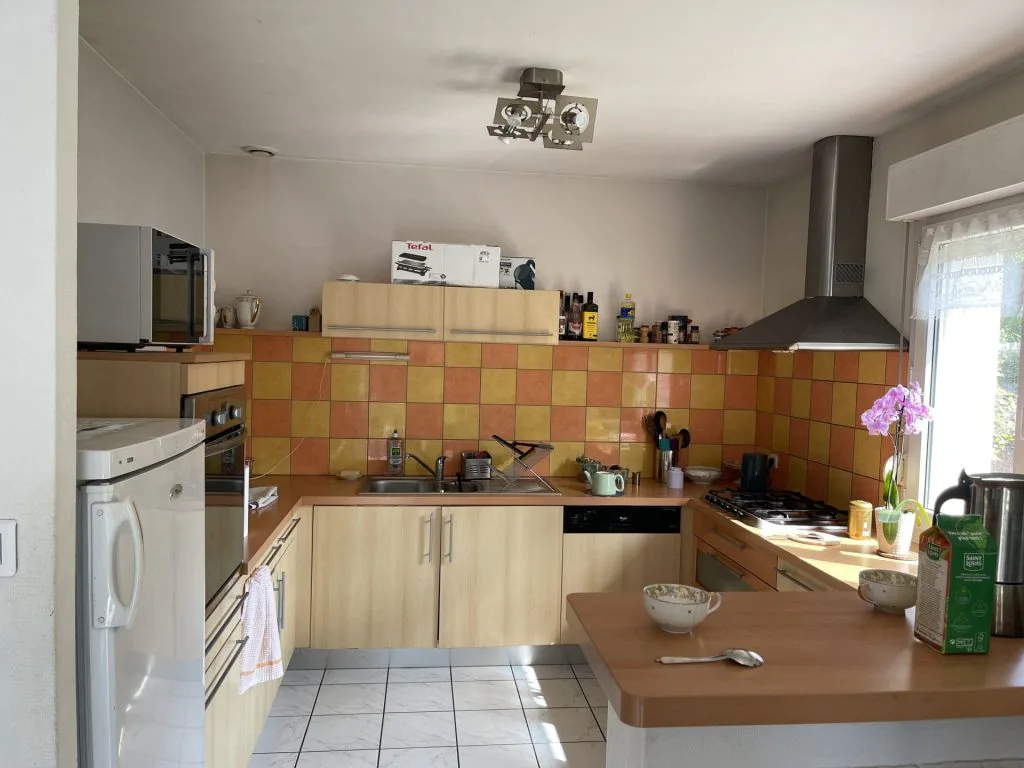 Ancienne cuisine avec meubles en bois clair et crédence à carreaux jaunes et orange