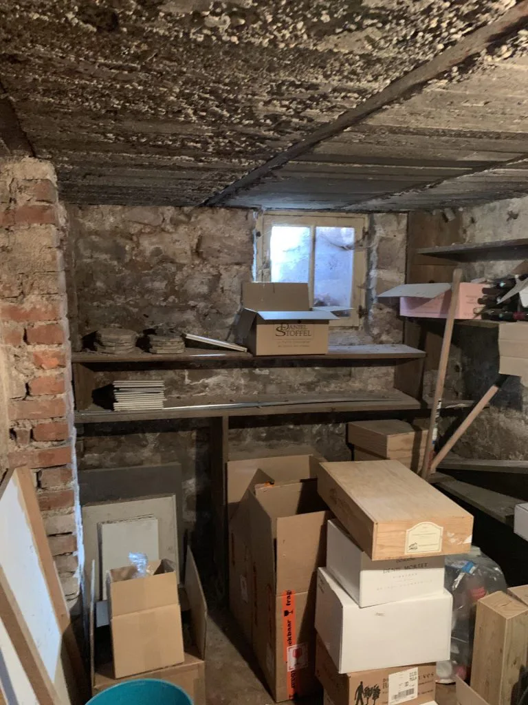 Ancienne pièce de cave utilisée comme stockage, avec étagères et fenêtre haute