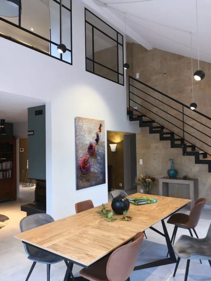 Salle à manger rénovée avec table en bois, escalier noir et mezzanine vitrée
