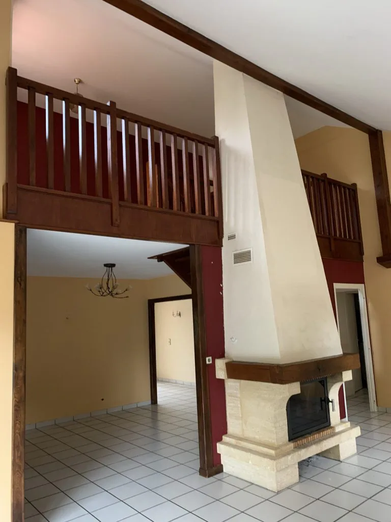 Ancienne pièce de vie avec cheminée centrale et mezzanine à garde-corps en bois