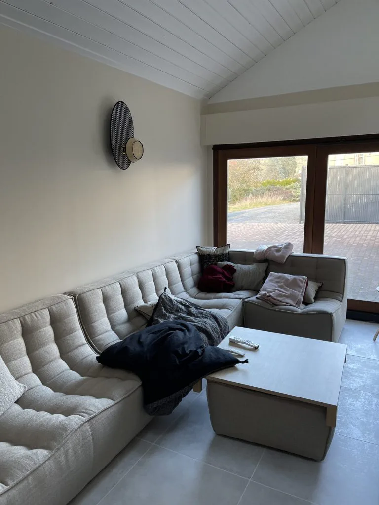 Salon rénové avec canapé gris, plafond clair et baie vitrée