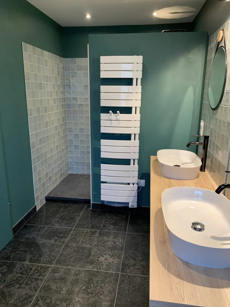 Salle d’eau rénovée avec douche ouverte, sèche-serviettes blanc et double vasque