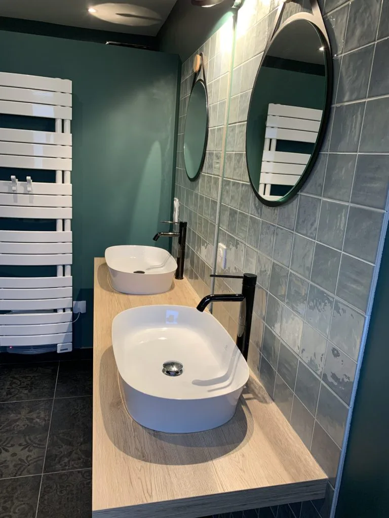 Double vasque blanche sur meuble en bois devant un carrelage bleu-vert
