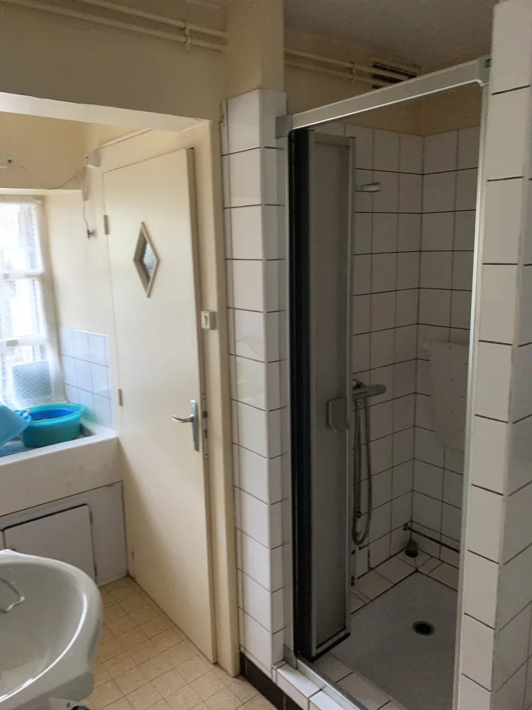 Ancienne salle de bains avec douche carrelée et petit meuble vasque