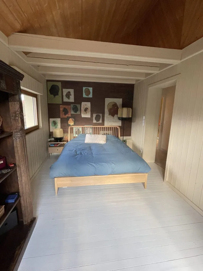 Chambre rénovée avec parquet clair, lit bleu et papier peint à motifs de portraits
