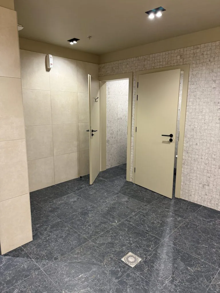 Cabines des sanitaires avec portes beiges, carrelage mural clair et sol gris foncé