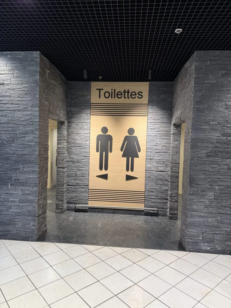 Entrée des toilettes avec signalétique dorée, pictogrammes et murs en parement gris