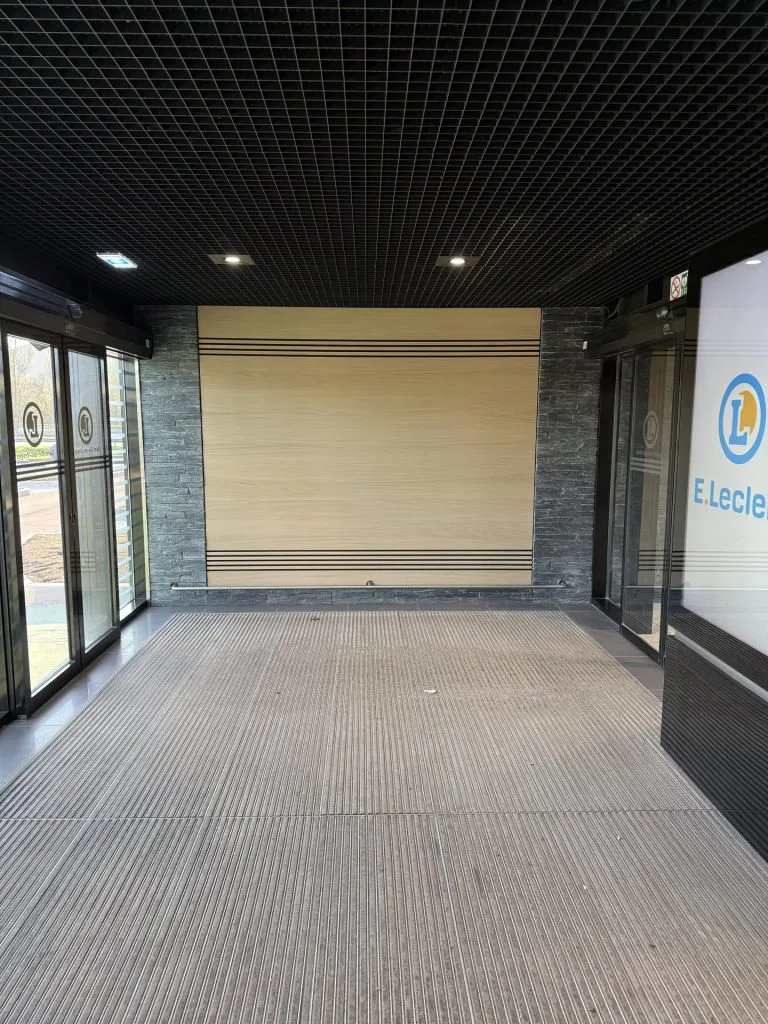 Entrée de la galerie du centre E.Leclerc avec plafond noir quadrillé et panneau mural en bois clair